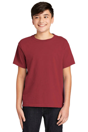 A teen boy smiles with hands by his sides, wearing a plain red Comfort Colors Youth Ring Spun T-Shirt 9018 and black pants, set against a white background.