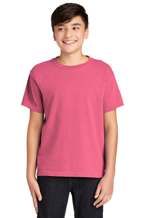 A teenage boy smiles in a Comfort Colors Youth Ring Spun T-Shirt 9018, made from 100% ring spun cotton, paired with dark pants against a white background.