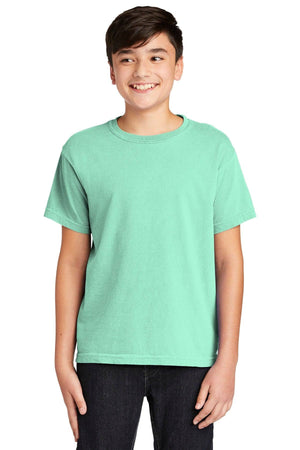 A person in a Comfort Colors Youth Ring Spun T-Shirt 9018, mint green and made of soft cotton, with black pants smiles warmly against a plain white background.