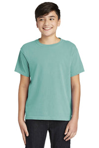 A teen in a Comfort Colors Youth Ring Spun T-Shirt 9018 with a vintage teal look and dark pants smiles against a plain white background.