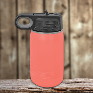 A red insulated stainless steel Kodiak Coolers water bottle with a black flip-top lid on a wooden surface against a blurred wooden backdrop, featuring vacuum-sealed insulation technology.