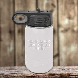 A matte white 12 oz Kodiak Coolers Custom Kids Water Bottle with black lid, engraved with "YOUR LOGO ENGRAVED HERE," sits on a wooden surface. Perfect for personalized logos or names—special Black Friday sale volume pricing, limited time!.