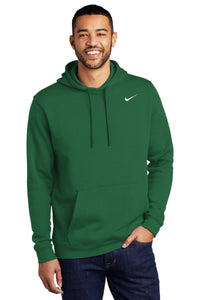 A person wearing a green Nike Club Fleece Pullover Hoodie Sweatshirt CJ1611, featuring an embroidered white Swoosh on the chest, stands against a white background, smiling with one hand in the hoodie pocket.