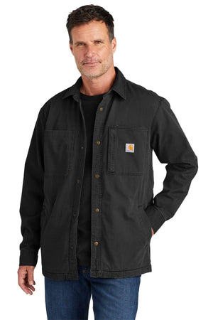 A man confidently stands against a plain white background, embodying the spirit of outdoor activities in a Carhartt Rugged Flex Fleece-Lined Shirt Jacket CT105532, paired with a black shirt and blue jeans.