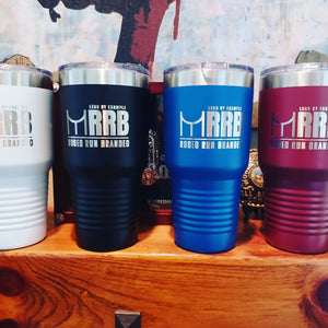 Four Kodiak Coolers insulated mugs in white, black, blue, and red with an engraved MRRB logo are arranged on a wooden shelf. These tumblers are ideal for any adventure and available at competitive wholesale prices. Minimal order: $250 during the Presidents Day Sale.
