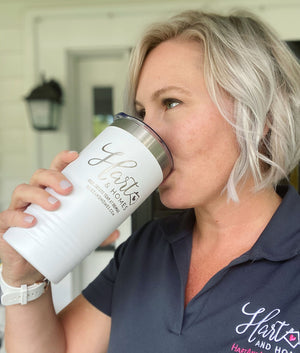 A short-haired blonde sips from a white Kodiak Coolers tumbler with an engraved logo, matching their dark collared shirt.