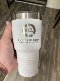 A hand holds a Kodiak Coolers custom tumbler showcasing a laser-engraved logo reading "ACL A Closer Look Home Inspection," set against a wooden floor backdrop.