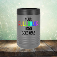 A silver Custom UV Printed Drinkware - ONE TIME SPECIAL OFFER with a black lid is displayed on a wooden surface against a blurry background. The text "Your Full Color Logo Goes Here" is printed on the drinkware in colorful letters, showcasing the perfect engraving option for tumblers and coffee mugs alike. This product is part of the Kodiak Coolers brand.