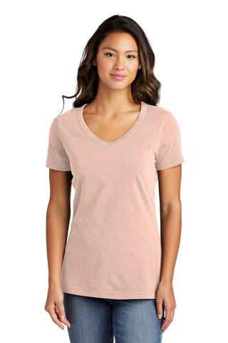 A person wearing a Port & Company Ladies Beach Wash Garment-Dyed V-Neck T-Shirt in pink, paired with blue jeans, stands against a plain white background.