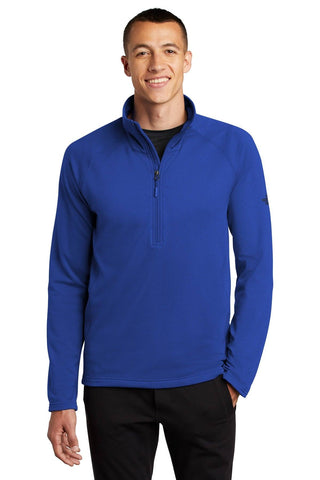 A man wearing The North Face Mountain Peaks 1/4-Zip Fleece Pullover NF0A47FB in blue and black pants stands facing forward, smiling against a plain white background.