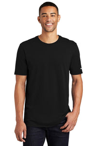 A smiling person is wearing a Nike Core Cotton T-Shirt NKBQ5233 in black and dark jeans, standing against a white background.