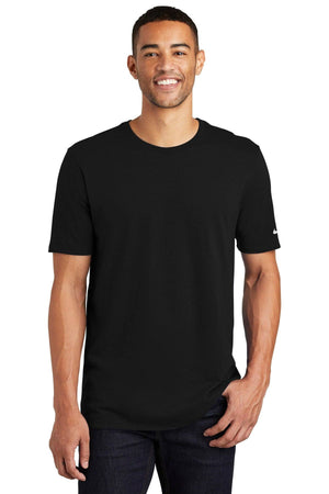 A smiling person is wearing a Nike Core Cotton T-Shirt NKBQ5233 in black and dark jeans, standing against a white background.