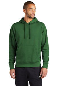 A person wearing a green Nike Club Fleece Sleeve Swoosh Pullover Hoodie Sweatshirt NKDR1499 and black pants, effortlessly capturing a casual street-ready look against a white background.