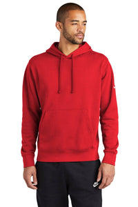 A man exudes a casual street-ready look in a Nike Club Fleece Sleeve Swoosh Pullover Hoodie Sweatshirt NKDR1499 in red with a front pocket, paired with black pants, standing confidently against a white background.