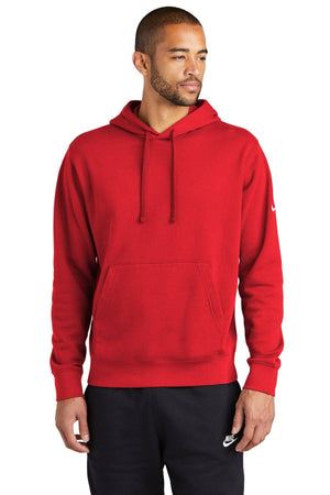 A man exudes a casual street-ready look in a Nike Club Fleece Sleeve Swoosh Pullover Hoodie Sweatshirt NKDR1499 in red with a front pocket, paired with black pants, standing confidently against a white background.