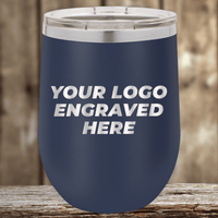 Kodiak Coolers' navy blue tumbler with a clear lid showcases "YOUR LOGO ENGRAVED HERE" in white—perfect as a Realtor closing gift or personalized company drinkware, set stylishly against a wooden background.