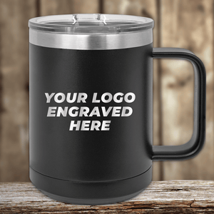 A black 15 oz Kodiak Coolers insulated mug with a silver lid sits elegantly on wood, featuring "YOUR LOGO ENGRAVED HERE" in white. Ideal for custom mugs or promotional gifts, each purchase includes a logo engraving and setup fee.