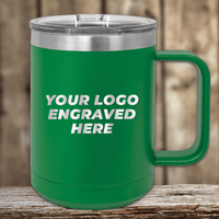 The green 15 oz insulated coffee mug by Kodiak Coolers features a clear lid and "YOUR LOGO ENGRAVED HERE" text, elegantly placed on a wooden surface. Ideal for promotional gifts, this custom mug allows your brand to stand out stylishly.