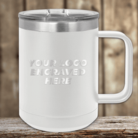 A SAMPLE 15 oz white Kodiak Coolers insulated mug with a silver handle and lid sits on a wooden surface, featuring "YOUR LOGO ENGRAVED HERE" text. Perfect for promotional gifts, this includes the engraved logo sample and volume setup fee.
