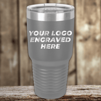 A gray insulated tumbler from Kodiak Coolers with your custom company logo engraved, shown with a clear lid on a wooden surface—an ideal Realtor Closing Gift or unique promotional drinkware for clients.