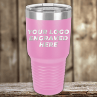 A pink Kodiak Coolers SAMPLE 30 oz tumbler with a clear lid, engraved with "YOUR LOGO ENGRAVED HERE" in white text—a perfect promotional drinkware item displayed on a wooden surface against a wood background.