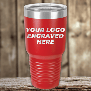 A red Kodiak Coolers SAMPLE 30 oz Tumbler with a clear lid rests on a wooden surface. "YOUR LOGO ENGRAVED HERE" appears on the front, ideal for personalized or promotional drinkware. Price includes engraved logo sample and setup fee.