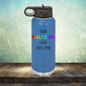 A blue stainless steel water bottle on a wooden surface with text "YOUR FULL COLOR LOGO GOES HERE" written on it. The background features a bokeh effect with light hues, similar to our selection of Kodiak Coolers Custom UV Printed Drinkware - Single Side Printing Included in Price for your branding needs.