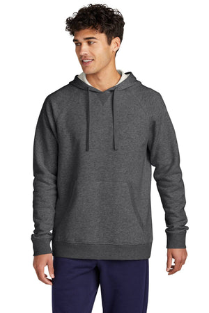 A person clad in a dark gray Sport-Tek Drive Fleece Pullover Hoodie Sweatshirt STF200 and dark pants stands against a white background. They are gazing to the side with curly hair, highlighting the comfortable fit of this cotton-rich fleece sweatshirt from Sport-Tek.