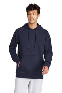 A person stands against a white background, wearing a Sport-Tek Drive Fleece Pullover Hoodie Sweatshirt STF200 in dark blue and light gray sweatpants.