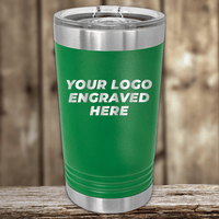 A green Kodiak Coolers tumbler with a clear lid displays "Your Custom Company Logo Engraved" on the front. Perfect as a Realtor closing gift for clients, it sits on wood with a blurred wooden background.