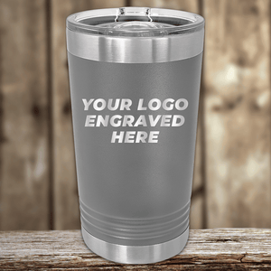 A gray stainless steel tumbler from Kodiak Coolers, customized with your company logo, makes the perfect Realtor Closing Gift. Displayed on a wooden surface with a blurred wooden background, ideal for promotional drinkware.