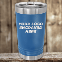 The Kodiak Coolers Realtor Closing Gifts for Clients tumbler features a blue insulated design with a clear lid and your custom company logo engraved on the front—perfect branded drinkware for client gifts, shown on a wooden surface with a blurred wood background.