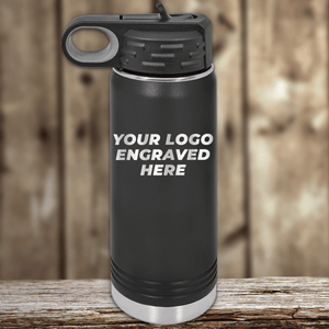 A black Kodiak Coolers bottle sits on a wooden surface, featuring "YOUR LOGO ENGRAVED HERE," making it a stylish Realtor Closing Gift for clients with your custom company logo on drinkware against a blurred wood background.
