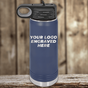 A blue stainless steel water bottle by Kodiak Coolers with a black lid, engraved with your custom company logo—ideal as Realtor Closing Gifts for Clients—displayed on a wooden surface with a blurred background.