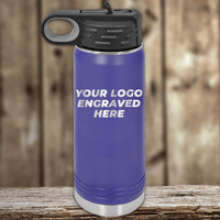 A blue Kodiak Coolers water bottle with a black lid sits on a wooden surface. Ideal as a realtor closing gift, it features "YOUR LOGO ENGRAVED HERE" showcasing your custom company logo on drinkware.