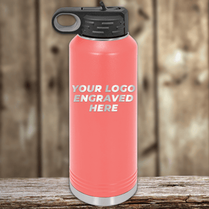 A pink Kodiak Coolers water bottle with a black lid rests on wood, featuring "YOUR LOGO ENGRAVED HERE" in white—Realtor Closing Gifts for Clients, perfect for custom logos and pairing with other promotional drinkware.