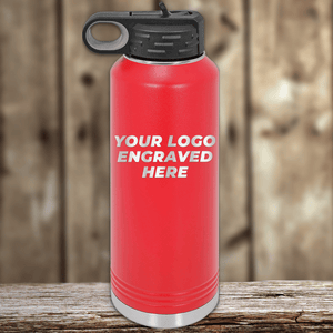 A Kodiak Coolers red metal water bottle with a black lid rests on a wooden surface, featuring your custom company logo engraved—perfect as Realtor Closing Gifts for Clients or personalized promotional drinkware.
