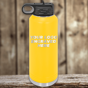 A yellow Kodiak Coolers water bottle with a black lid, engraved with "Your Custom Company Logo," sits on a wooden surface—perfect as a Realtor Closing Gift or for pairing with custom logo drinkware.