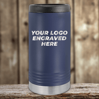 The Kodiak Coolers Realtor Closing Gifts for Clients tumbler features your custom company logo engraved, with a navy blue body, black lid, and silver bottom. It sits on a wooden surface against a blurred wood background.