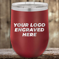 A red 12 oz Kodiak Coolers Custom Wine Cup with "YOUR LOGO ENGRAVED HERE" in white sits on wood. Perfect for custom logo engraving, now available at special Black Friday sale volume pricing for a limited time!.