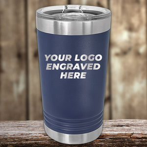 A blue Kodiak Coolers tumbler with a clear lid on a wooden surface displays "YOUR LOGO ENGRAVED HERE." Perfect for custom drinkware, it features laser logo engraving. Enjoy no setup fee and a $250 minimum order during the special Presidents Day sale. The background is blurred wood.