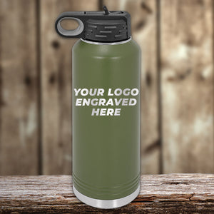 A green Kodiak Coolers insulated water bottle featuring a black lid and loop handle, rests on a wooden surface. The text reads "Your Laser Engraved Logo Here." A blurred wooden wall serves as the backdrop. Ideal for custom tumblers at wholesale pricing, with no setup fee and 1 side logo included.
