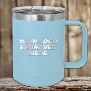 A light blue 15 oz insulated stainless steel coffee mug by Kodiak Coolers sits on a wooden surface, featuring custom laser-engraved text "YOUR LOGO ENGRAVED HERE" in white capital letters. Available with special bulk wholesale pricing.