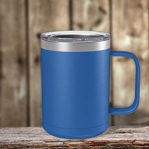 A blue insulated stainless steel coffee mug with a Kodiak Coolers logo engraved by laser, resting on a wooden table.