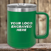 A 15 oz green Kodiak Coolers Custom Coffee Mug with handle and clear lid, laser-engraved with "YOUR LOGO ENGRAVED HERE" on the front. The mug sits on a wooden surface, perfect for Black Friday Sale volume pricing—LIMITED TIME offer!.