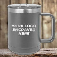 The Kodiak Coolers 15 oz gray stainless steel coffee mug features a laser-engraved "Your Logo Here" text, complete with a clear lid, on a wooden surface. Available with special bulk wholesale pricing.