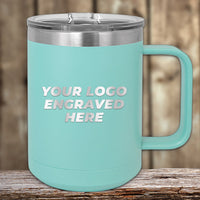 A teal Kodiak Coolers 15 oz stainless steel insulated mug sits on wood, featuring a clear lid and laser-engraved "Your Logo Engraved Here." Blurred wooden planks in the background enhance the cozy setting ideal for custom coffee mugs.