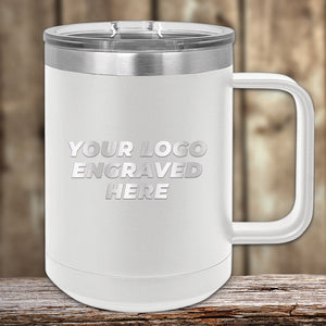 The 15 oz white insulated mug from Kodiak Coolers sits on a wooden table, displaying "Your Logo Engraved Here" on its side. This custom mug offers a sleek look, with your logo laser-engraved for personalized charm against the blurred wooden wall backdrop.
