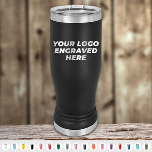 A 14 oz Kodiak Coolers Custom Pilsner Glass in black stainless steel with silver accents sits on a wooden surface, displaying "YOUR LOGO ENGRAVED HERE." Multiple color choices for these engraved tumblers are available at the bottom.