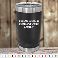 A Kodiak Coolers black insulated tumbler with a laser-engraved "YOUR LOGO ENGRAVED HERE" sits on wood among diverse colors. Ideal for custom orders with no setup fees and attractive wholesale pricing during the Presidents Day sale. Note: $250 minimum order required.